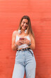 © Julio Rodriguez/Westend61 - Smiling woman using mobile phone standing in front of orange wall