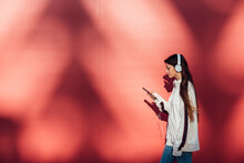 Teenage girl using mobile phone while walking by red wall