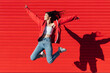 © Julio Rodriguez/Westend61 - Smiling teenage girl with arms outstretched jumping in front of red wall