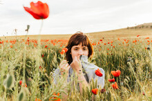 Mid Adult Woman Covering Mouth With Shirt While Sitting At Poppy Field