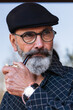 © NOVELLIMAGE/Westend61 - Bearded man in flat hat looking away while holding smoking pipe