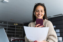 Smiling Young Businesswoman With Document Sending Voicemail On Smart Phone At Office