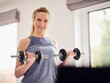 © Phillip Waterman/Westend61 - Smiling woman holding weights while exercising at home