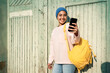 © Rafa Cortes/Westend61 - Smiling woman with backpack taking selfie through smart phone during sunny day