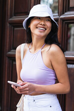 Smiling Young Woman Wearing Bucket Hat Holding Smart Phone Outdoors