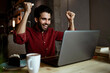 © Rafa Cortes/Westend61 - Businessman cheering while looking at laptop while sitting in illuminated coffee shop