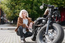 Mature Woman Crouching By Motorcycle On Sunny Day