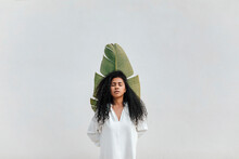 Young Woman With Eyes Closed Holding Banana Leaf In Front Of White Wall