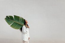 Young Woman Carrying Big Banana Leaf By White Wall