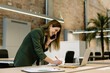 © Xavier Lorenzo/Westend61 - Cheerful businesswoman talking on smart phone while writing in diary by laptop at office