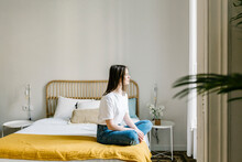 Contemplating young woman looking away while sitting on bed at home