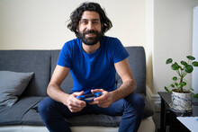 Smiling Man With Game Controller Sitting On Sofa At Home