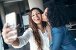 © JOSEP SURIA/Westend61 - Smiling businesswoman taking selfie while being kissed by female colleague in office