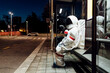 © Eugenio Marongiu/Westend61 - Young female astronaut in space suit waiting at bus stop during night