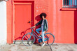 © Eugenio Marongiu/Westend61 - Smiling woman standing with bicycle by red building