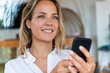 © steve brookland/Westend61 - Smiling beautiful woman holding mobile phone at home