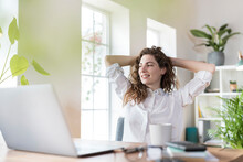 Smiling Female Professional With Hands Behind Head Relaxing At Desk In Home Office