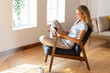 © steve brookland/Westend61 - Smiling woman using digital tablet while sitting on chair in living room