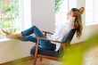 © steve brookland/Westend61 - Relaxed woman with arms raised sitting on chair at home