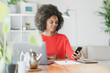 © steve brookland/Westend61 - Young woman using mobile phone while sitting by laptop at home