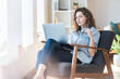© steve brookland/Westend61 - Thoughtful young woman holding eyeglasses while looking at laptop on chair at home