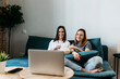 © Xavier Lorenzo/Westend61 - Smiling young girlfriends watching movie on laptop while eating popcorn