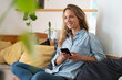 © steve brookland/Westend61 - Smiling woman with smart phone relaxing on couch in living room