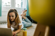 © Xavier Lorenzo/Westend61 - Smiling woman using laptop while lying on carpet at home