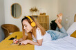 © Xavier Lorenzo/Westend61 - Redheaded woman writing on note pad while listening music on bed at home