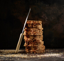 Studio shot of kitchen knife leaning on stack of fresh wholegrain bread slices