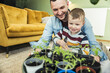 © Uwe Umstatter/Westend61 - Cute boy spraying water on potted plants while sitting with father in living room at home