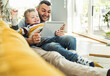 © Uwe Umstatter/Westend61 - Smiling father and son watching video through tablet while sitting on sofa in living room