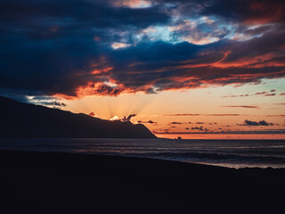 Wall Mural - Beautiful sea with coastline hills under a cloudy sky at sunset