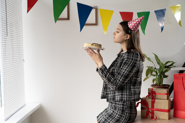 birthday in the office. A young Caucasian lady holds a birthday cake in her hands and blows out the fire.