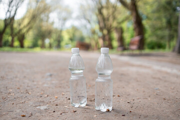 Two plastic bottles of fresh water standing on road at green summer park. Mineral liquid preparing for sportsmen tp refreshing after run. Water balance and sport concept.