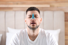 Man With Clothespin Suffering From Runny Nose In Bedroom