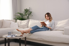 Young Woman Reading Book On Sofa At Home
