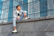 Handsome young guy in stylish clothes sits on glass facade background. Young man in city. Student resting after study