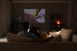 Couple watching movie on sofa at night, back view. Space for text
