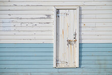 White Rusting Door On Blue And White Paneling On A Port Building.