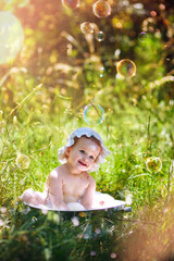 Cute little girl sits in a basin of summer water with foam on the green grass.	