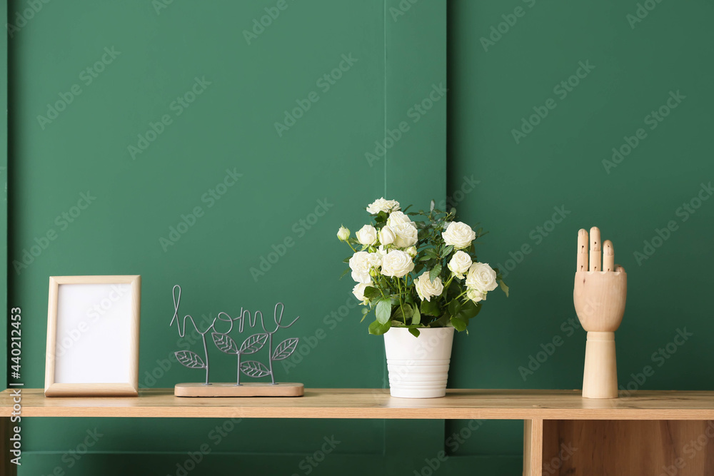 Beautiful white rose in pot and decor on table near color wall