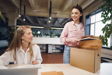 Young businesswoman holding box of personal belongings about to leave office after quitting job