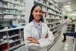 © StratfordProductions - Portrait of young african american pharmacist standing between aisle in chemist with colleague working in background