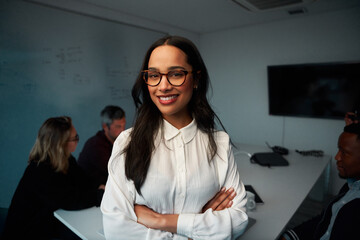 Portrait of a young confident businesswoman with her hands crossed standing in meeting room