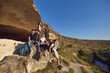 © Studio Romantic - Hiking and traveling together. Group of happy young friends hikers having rest on natural rocks and enjoying green valley landscape during summer vacations on sunny clear day, side view