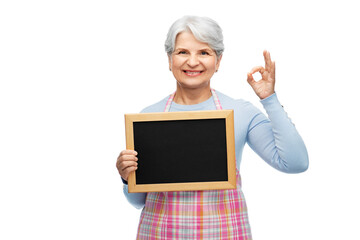 Poster - cooking, culinary and old people concept - portrait of smiling senior woman in kitchen apron holding chalkboard and showing ok gesture over white background