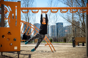 Wall Mural - Cute boy is climbing on the playground in the schoolyard. He has a very happy face and enjoy this adventure sports alone outdoor. Warm sunny day