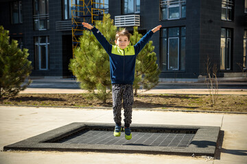 Little boy playing on the field at the day time. People having fun outdoors. He jumping on trampoline on the lawn. Concept of friendly family