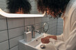 © Daniel - Young mixed race woman washing hands and face in a modern washroom. Curly hair female getting ready in the morning.
